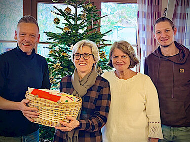 Gruppenbild vor einen Weihnachtsbaum, die Postkarten werden in einem Korb übergeben.