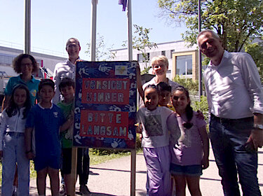 Gruppenbild mit allen Beteiligten und dem Plakat vor der Grundschule Süd