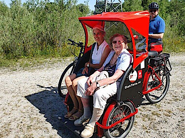 Zwei Passagierinnen und der Fahrer bei einem Ausflug mit der Rikscha ins Grüne