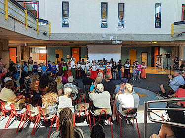 Im Vordergrund das Publikum, im Hintergrund Bürgermeister Seidl mit vielen Teilnehmerinnen und Teilnehmern bei der Aufführung in der Aula der Grundschule Süd Im Vordergrund das Publikum, im Hintergrund Bürgermeister Seidl mit vielen Teilnehmerinnen und Teilnehmern bei der Aufführung in der Aula der Grundschule Süd