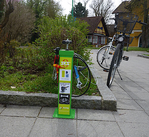 Fahrradreparaturstation mit Werkzeug und Luftpumpe, daneben steht ein Fahrrad