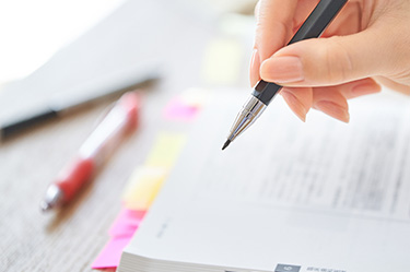Hand mit Stift über einem Buch mit Post-its Hand mit Stift über einem Buch mit Post-its